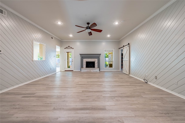 unfurnished living room featuring a barn door, light hardwood / wood-style floors, ceiling fan, and crown molding