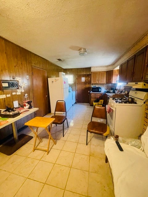 kitchen featuring light tile patterned floors, white appliances, a textured ceiling, and wood walls