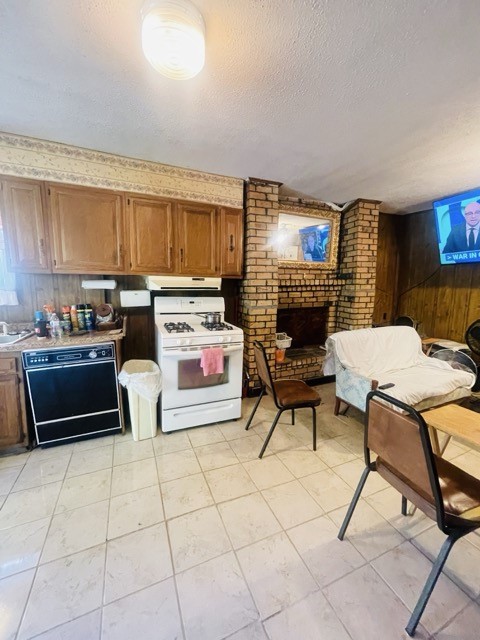 kitchen featuring dishwasher, a brick fireplace, white range with gas cooktop, and a textured ceiling