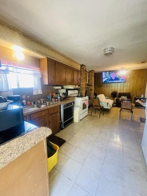 kitchen with white gas range, wooden walls, sink, and black dishwasher