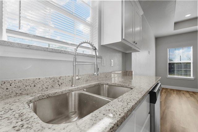 kitchen with light stone counters, stainless steel dishwasher, sink, hardwood / wood-style flooring, and white cabinets