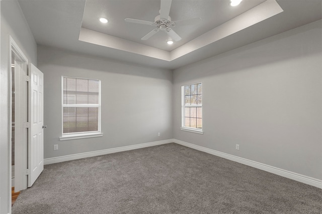 carpeted spare room featuring a tray ceiling and ceiling fan