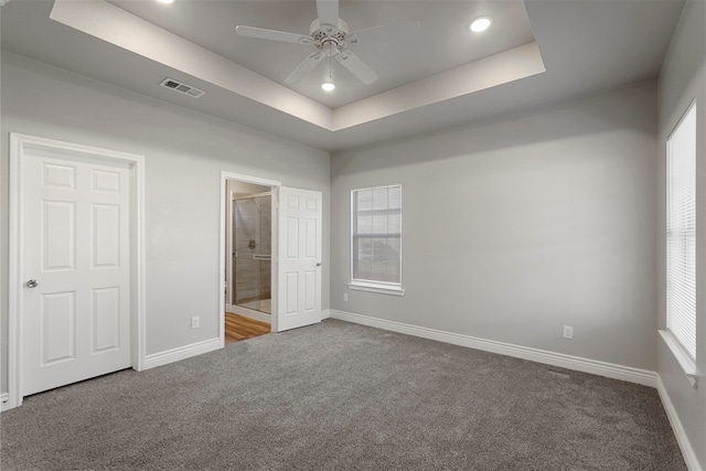 unfurnished bedroom with carpet floors, ensuite bathroom, a tray ceiling, and ceiling fan