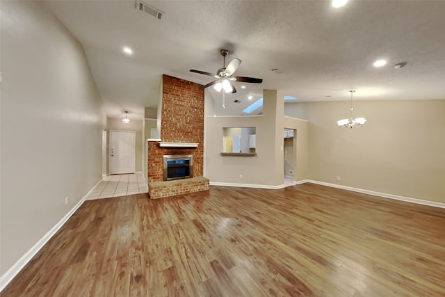 unfurnished living room with vaulted ceiling, ceiling fan with notable chandelier, a fireplace, a textured ceiling, and light wood-type flooring