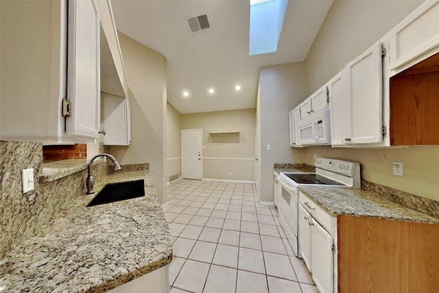 kitchen featuring a skylight, white appliances, sink, light tile patterned floors, and white cabinetry