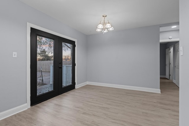 empty room with a chandelier, french doors, and light hardwood / wood-style floors