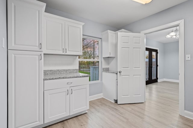 kitchen with decorative backsplash, light stone countertops, an inviting chandelier, white cabinets, and light hardwood / wood-style floors