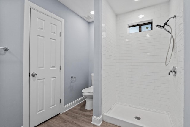 bathroom with hardwood / wood-style floors, toilet, and tiled shower