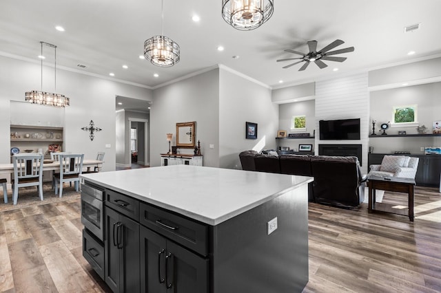 kitchen with hardwood / wood-style flooring, ceiling fan with notable chandelier, a center island, stainless steel microwave, and decorative light fixtures