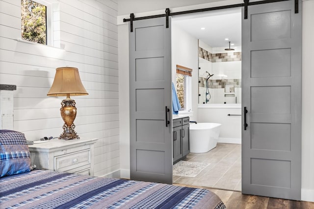 bedroom featuring ensuite bathroom, a barn door, and wood-type flooring