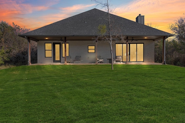 back house at dusk with a lawn, ceiling fan, and a patio area