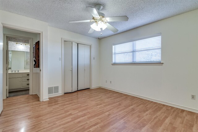 unfurnished bedroom with a textured ceiling, light wood-type flooring, ensuite bath, and ceiling fan