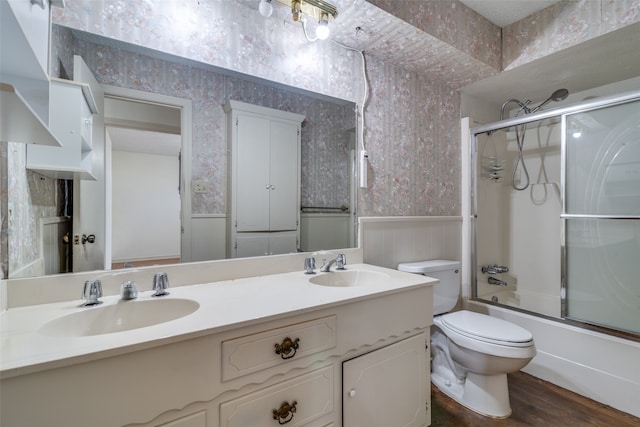 full bathroom featuring hardwood / wood-style flooring, vanity, shower / bath combination with glass door, and toilet