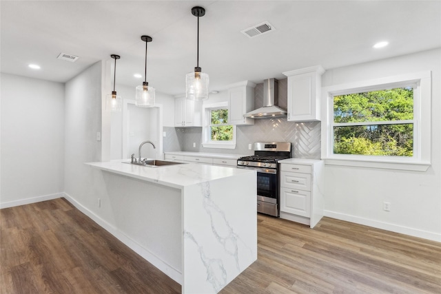 kitchen featuring decorative light fixtures, wall chimney range hood, sink, stainless steel range with gas cooktop, and white cabinets