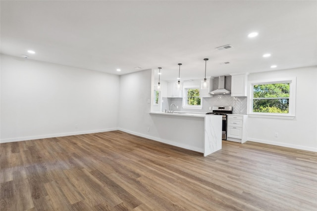 kitchen with white cabinetry, kitchen peninsula, pendant lighting, wall chimney range hood, and stainless steel stove