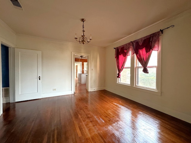 empty room featuring wood-type flooring, ornamental molding, and a notable chandelier