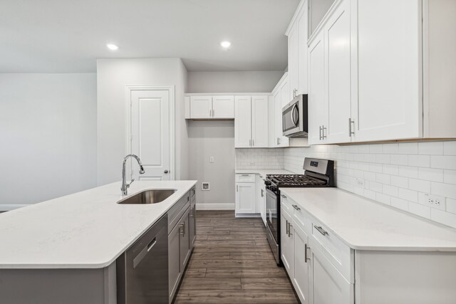 kitchen with appliances with stainless steel finishes, a kitchen island with sink, sink, light hardwood / wood-style flooring, and white cabinets