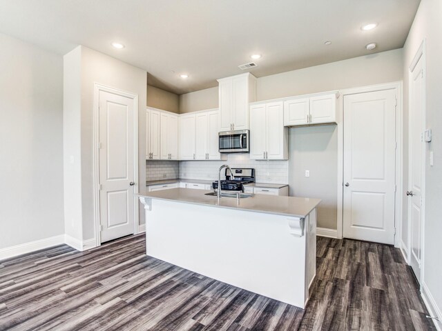 kitchen with appliances with stainless steel finishes, dark hardwood / wood-style flooring, a kitchen island with sink, sink, and white cabinetry