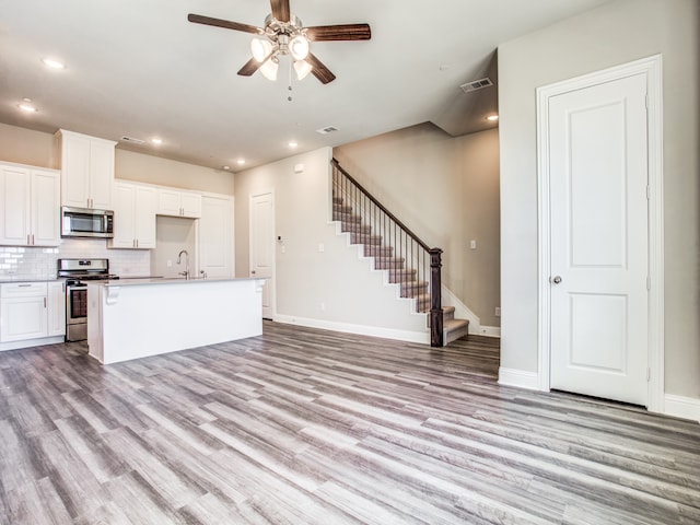 kitchen with a kitchen island with sink, white cabinets, light hardwood / wood-style flooring, ceiling fan, and stainless steel appliances