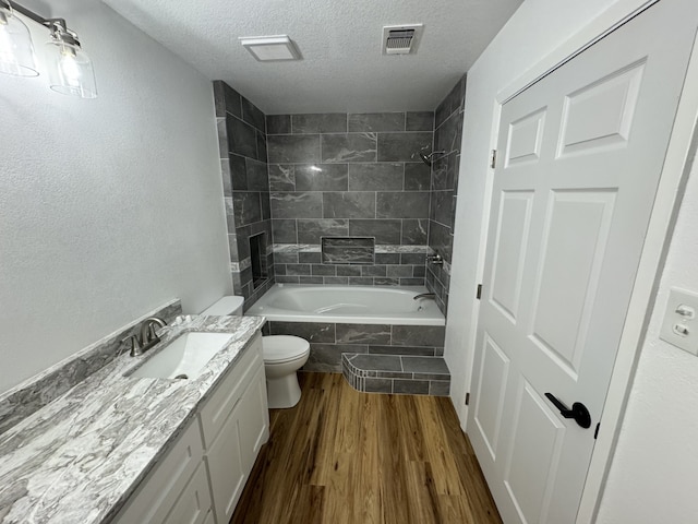 full bathroom featuring vanity, wood-type flooring, a textured ceiling, tiled shower / bath, and toilet