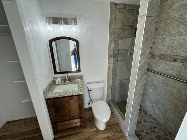 bathroom featuring toilet, a tile shower, wood-type flooring, and vanity