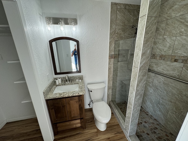 bathroom featuring vanity, hardwood / wood-style flooring, toilet, and tiled shower