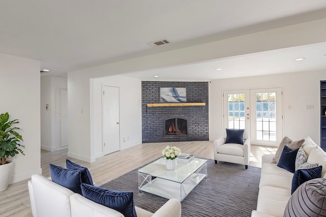 living room with french doors, light hardwood / wood-style floors, and a brick fireplace