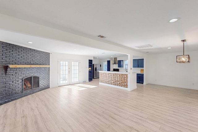 unfurnished living room with french doors, light hardwood / wood-style floors, brick wall, and a brick fireplace