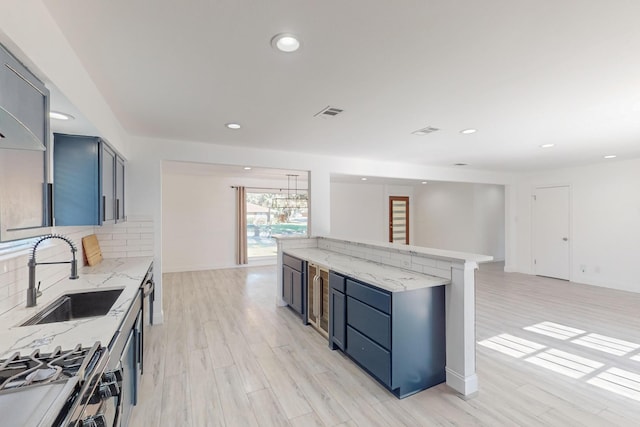 kitchen with sink, light hardwood / wood-style flooring, decorative backsplash, stainless steel range, and light stone counters