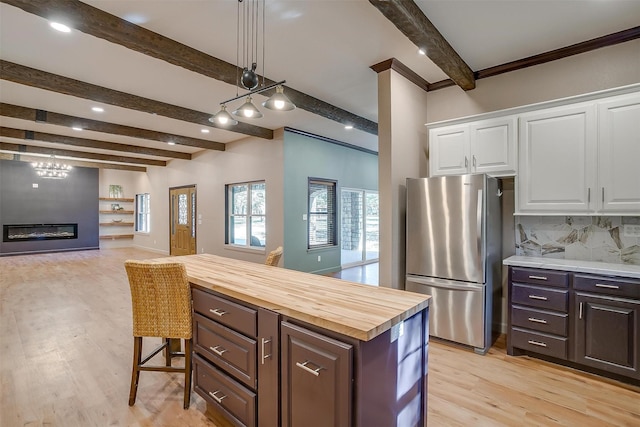 kitchen featuring butcher block counters, beamed ceiling, stainless steel fridge, a breakfast bar area, and white cabinets