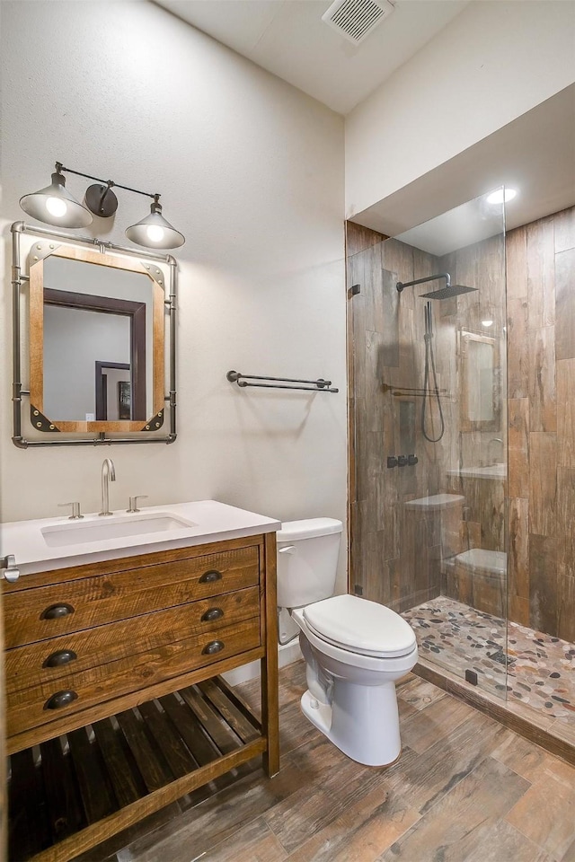 bathroom featuring hardwood / wood-style floors, toilet, a tile shower, and vanity