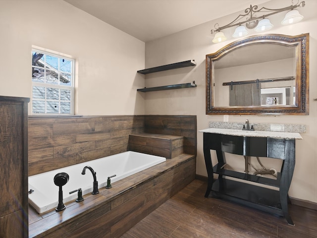 bathroom with hardwood / wood-style flooring, vanity, and a relaxing tiled tub