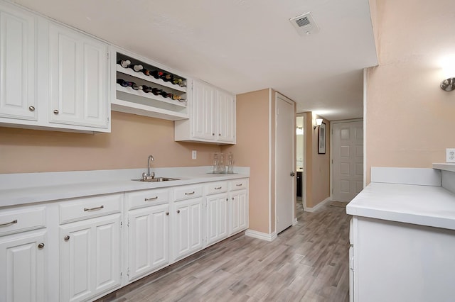 kitchen with light countertops, visible vents, white cabinets, a sink, and light wood-type flooring