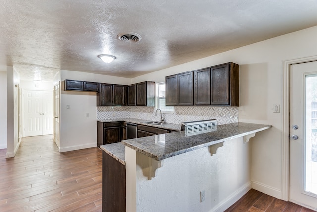 kitchen featuring a breakfast bar, backsplash, dark stone counters, and kitchen peninsula