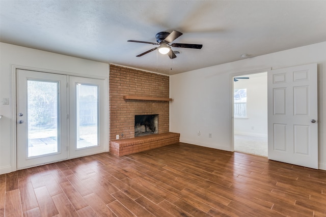 unfurnished living room featuring a brick fireplace, dark wood-type flooring, a textured ceiling, and ceiling fan