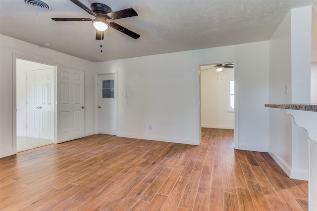 unfurnished room with ceiling fan, a textured ceiling, and light wood-type flooring