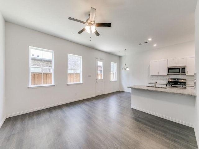 kitchen featuring appliances with stainless steel finishes, tasteful backsplash, white cabinetry, hanging light fixtures, and light stone counters