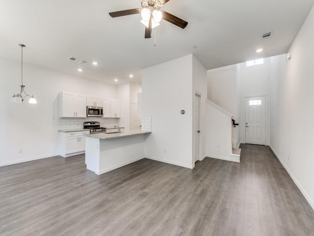 kitchen with appliances with stainless steel finishes, white cabinetry, hardwood / wood-style floors, light stone counters, and kitchen peninsula