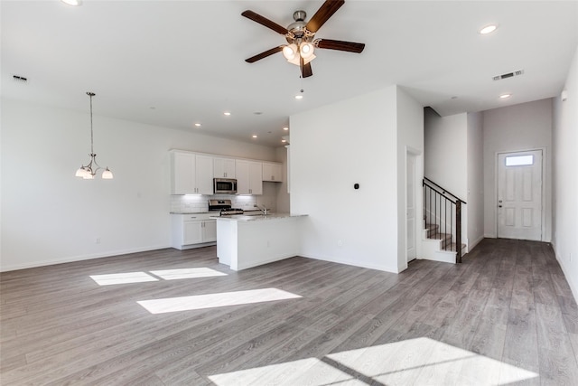 unfurnished living room with sink, ceiling fan with notable chandelier, and light wood-type flooring