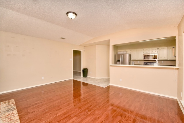 unfurnished living room with a textured ceiling, light hardwood / wood-style flooring, and vaulted ceiling