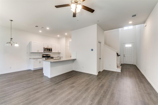 kitchen with stainless steel appliances, light stone counters, kitchen peninsula, wood-type flooring, and white cabinets