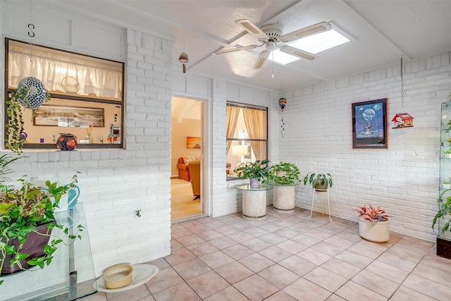 interior space featuring ceiling fan, light tile patterned flooring, and brick wall