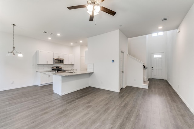 kitchen with kitchen peninsula, light stone counters, stainless steel appliances, wood-type flooring, and white cabinets