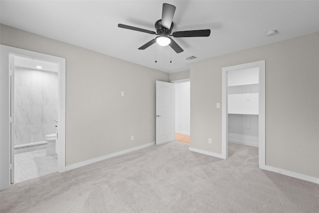 unfurnished bedroom featuring ensuite bathroom, ceiling fan, a walk in closet, and light carpet