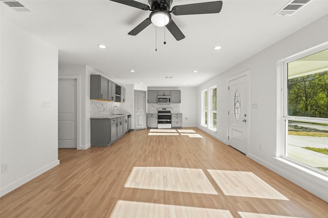 unfurnished living room featuring light wood-type flooring, ceiling fan, a healthy amount of sunlight, and sink