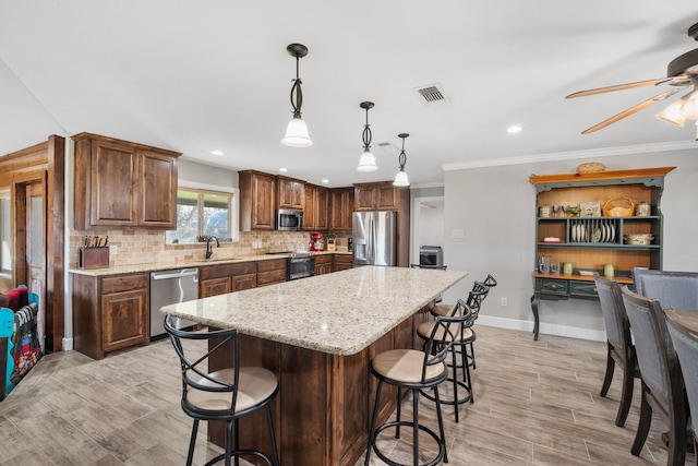 kitchen with a kitchen island, backsplash, hanging light fixtures, stainless steel appliances, and light stone countertops