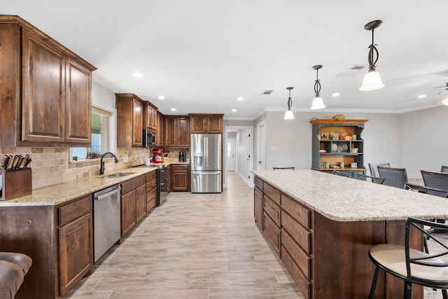 kitchen with a kitchen bar, sink, appliances with stainless steel finishes, a kitchen island, and pendant lighting