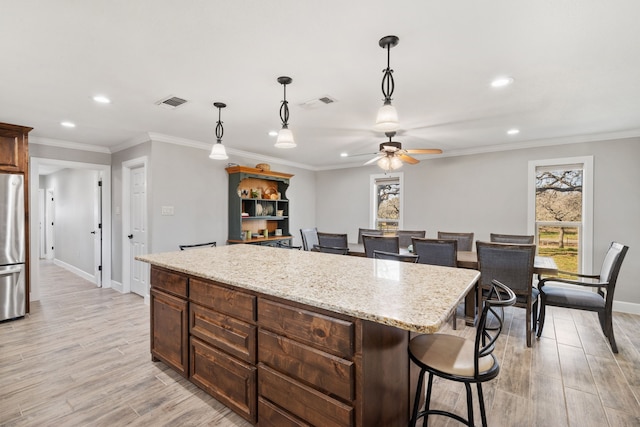 kitchen featuring a kitchen island, stainless steel refrigerator, light stone counters, crown molding, and light hardwood / wood-style flooring