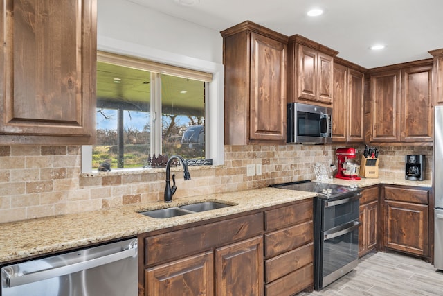 kitchen featuring appliances with stainless steel finishes, sink, decorative backsplash, light stone countertops, and light wood-type flooring