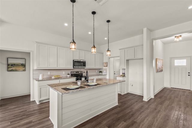 kitchen featuring a kitchen island with sink, light stone countertops, dark hardwood / wood-style flooring, white cabinetry, and stainless steel appliances